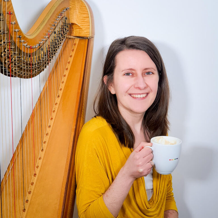 Zuzanna next to her harp, holding a cup of coffee
